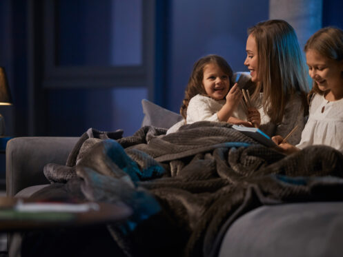 Mom and daughters curled up under a blanket during reading time